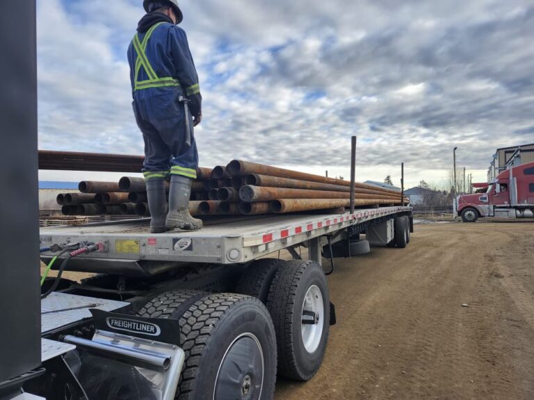 man loading oilfield pipe onto truck trailer